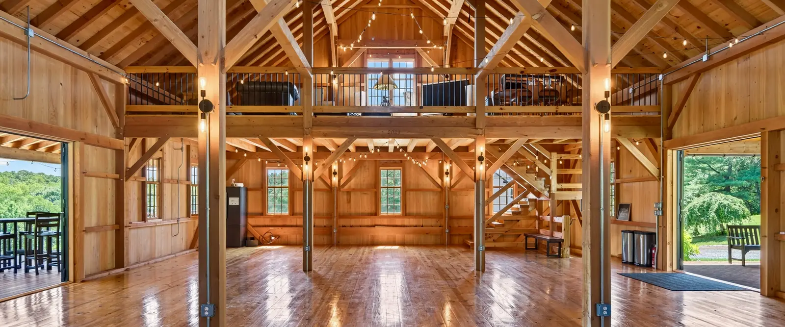 Open barn interior with vaulted trusses, loft, and dual staircases