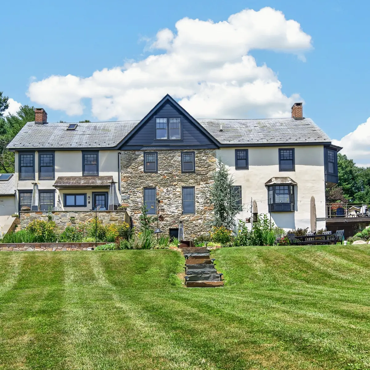 Rear elevation of the Farmhouse across the mowed lawn, with stone terrace and gardens