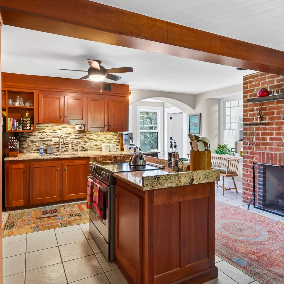 Kitchen with cherry cabinetry, stone backsplash, and view to the brick fireplace